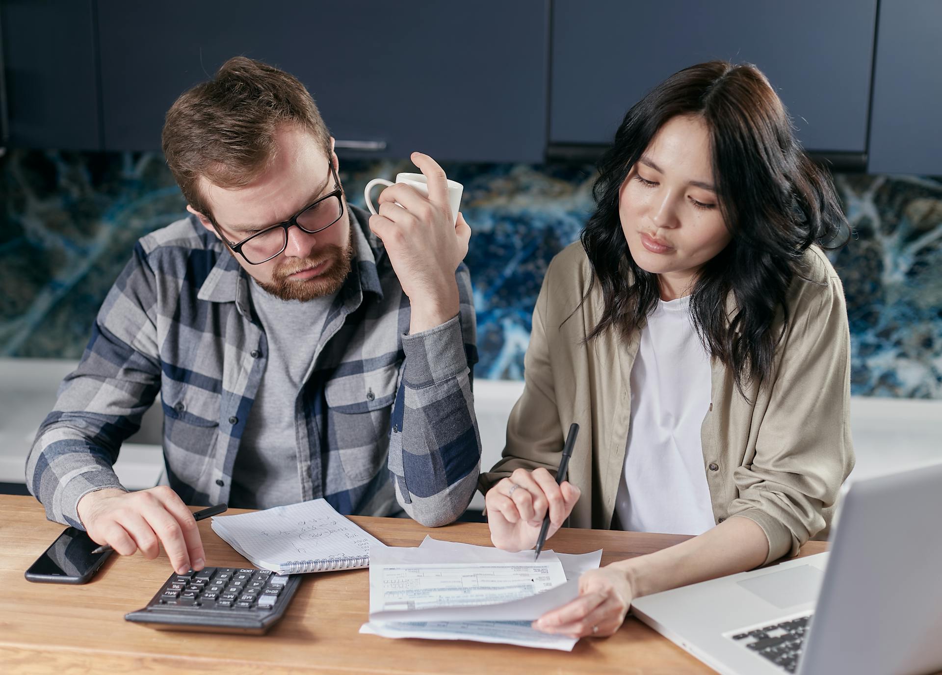 A couple reviewing mortgage paperwork and a calculator at the kitchen counter