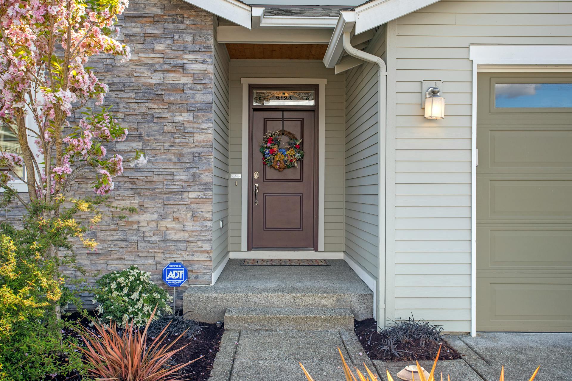Welcoming front entry featuring stone veneer, brown door with wreath, and flower, representative of the mature inner-city streetscapes around Inglewood, Edmonton