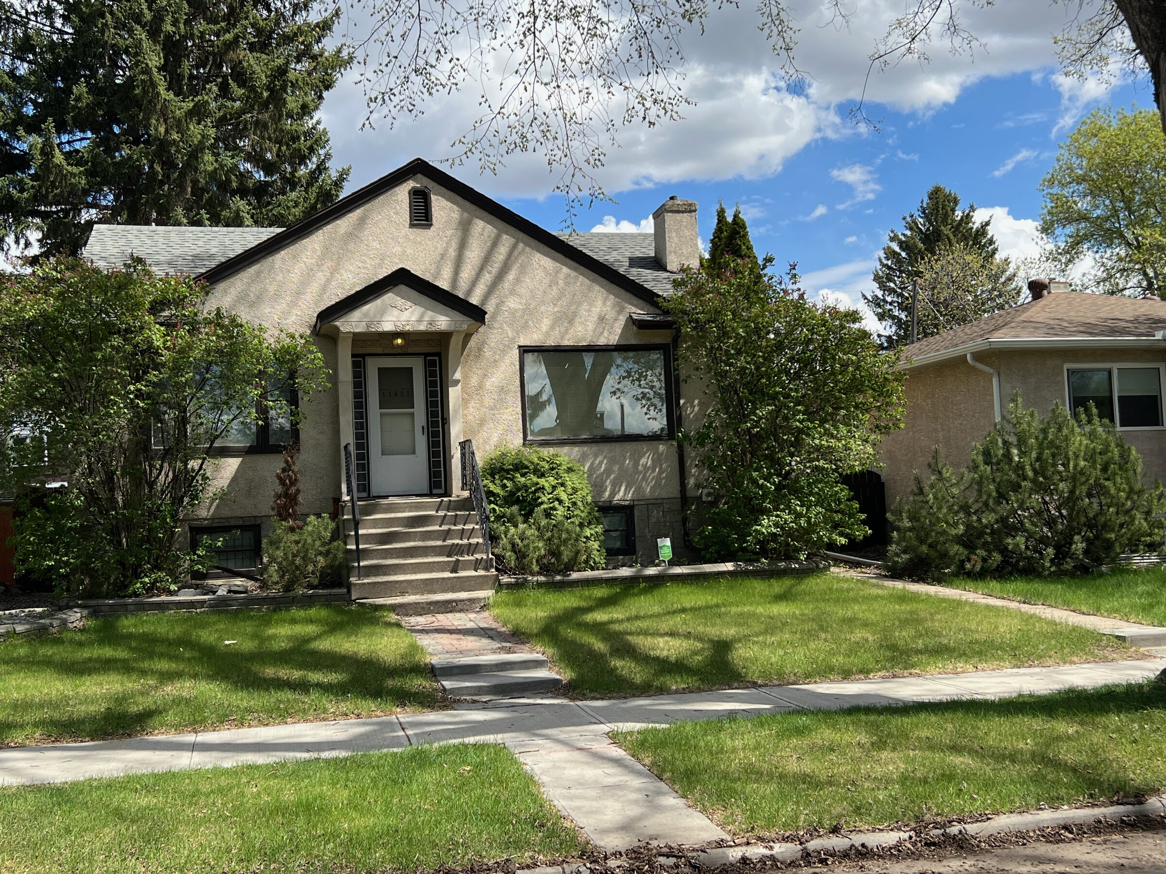 Post-war stucco bungalow with mature trees and a landscaped front yard on a Westmount residential street in Edmonton