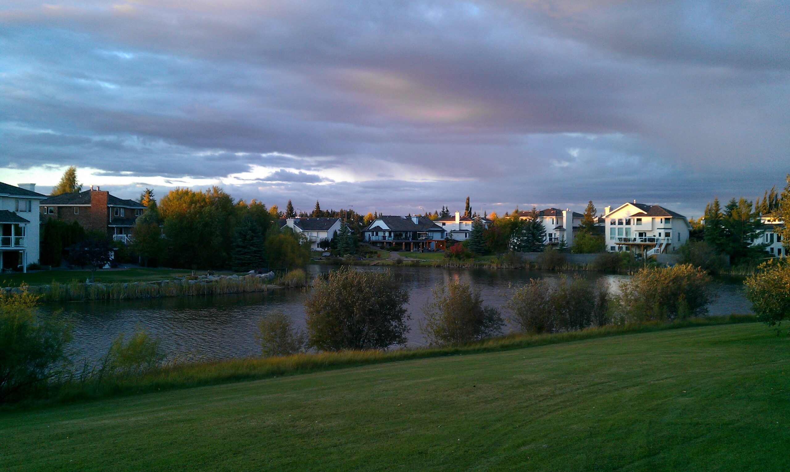 Detached homes surrounding a residential lake under autumn foliage at dusk, illustrative of lake-community living of the kind found in Summerside, Edmonton